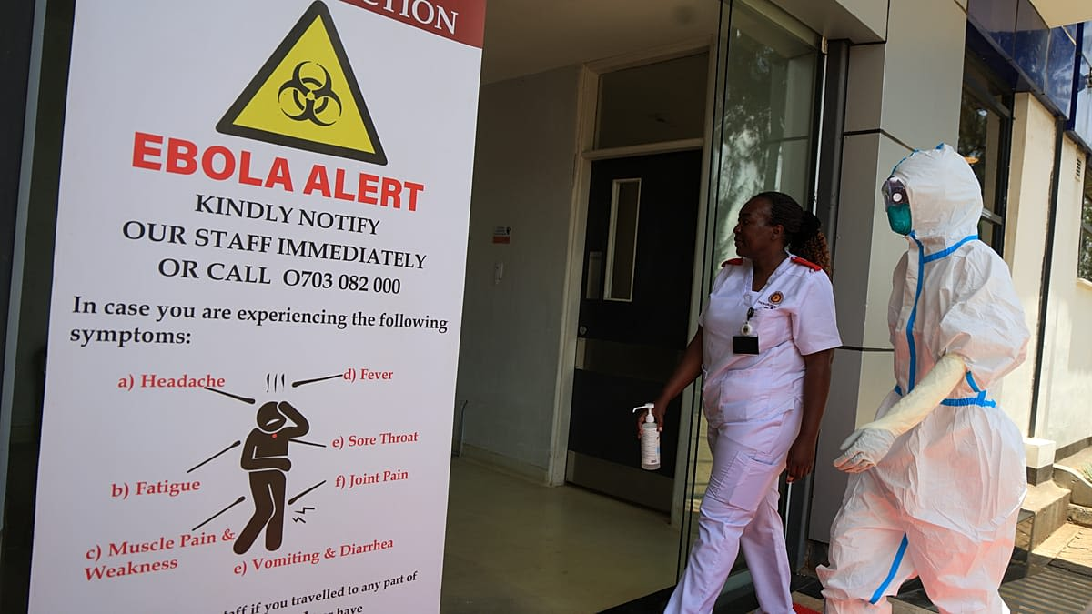 Healthcare workers beside an Ebola alert sign, including one wearing protective equipment